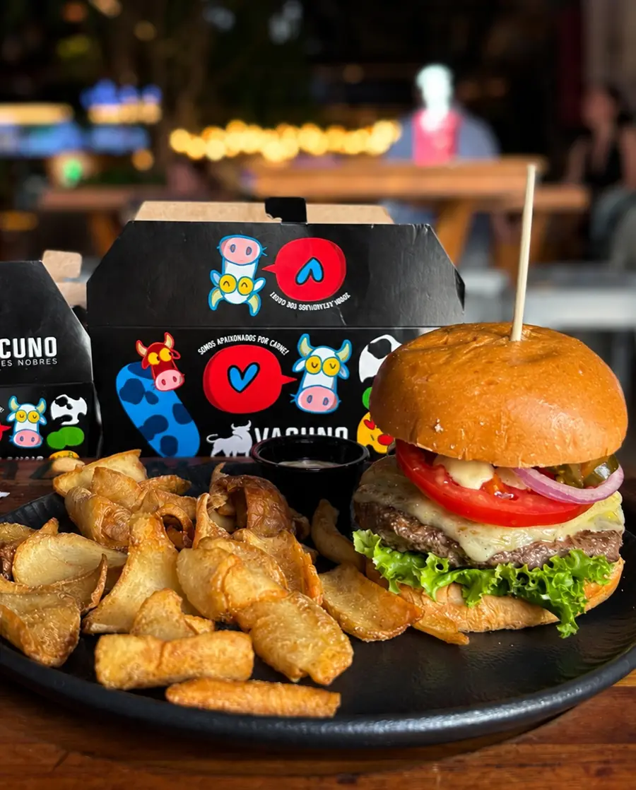 Caixa de delivery do Vacuno com a arte de Luciano Martins, ao lado de um cheeseburger